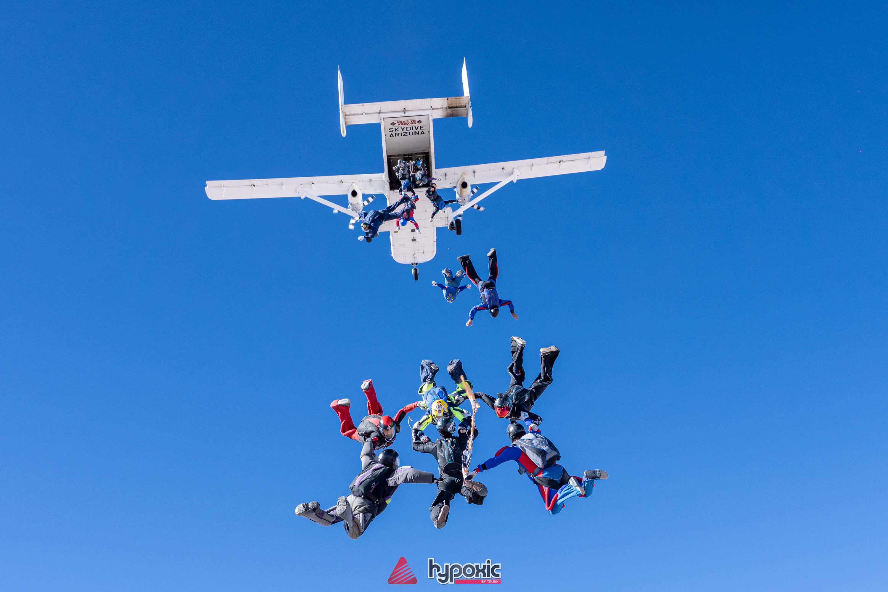 Skydivers building a formation below a jump plane in a clear blue sky