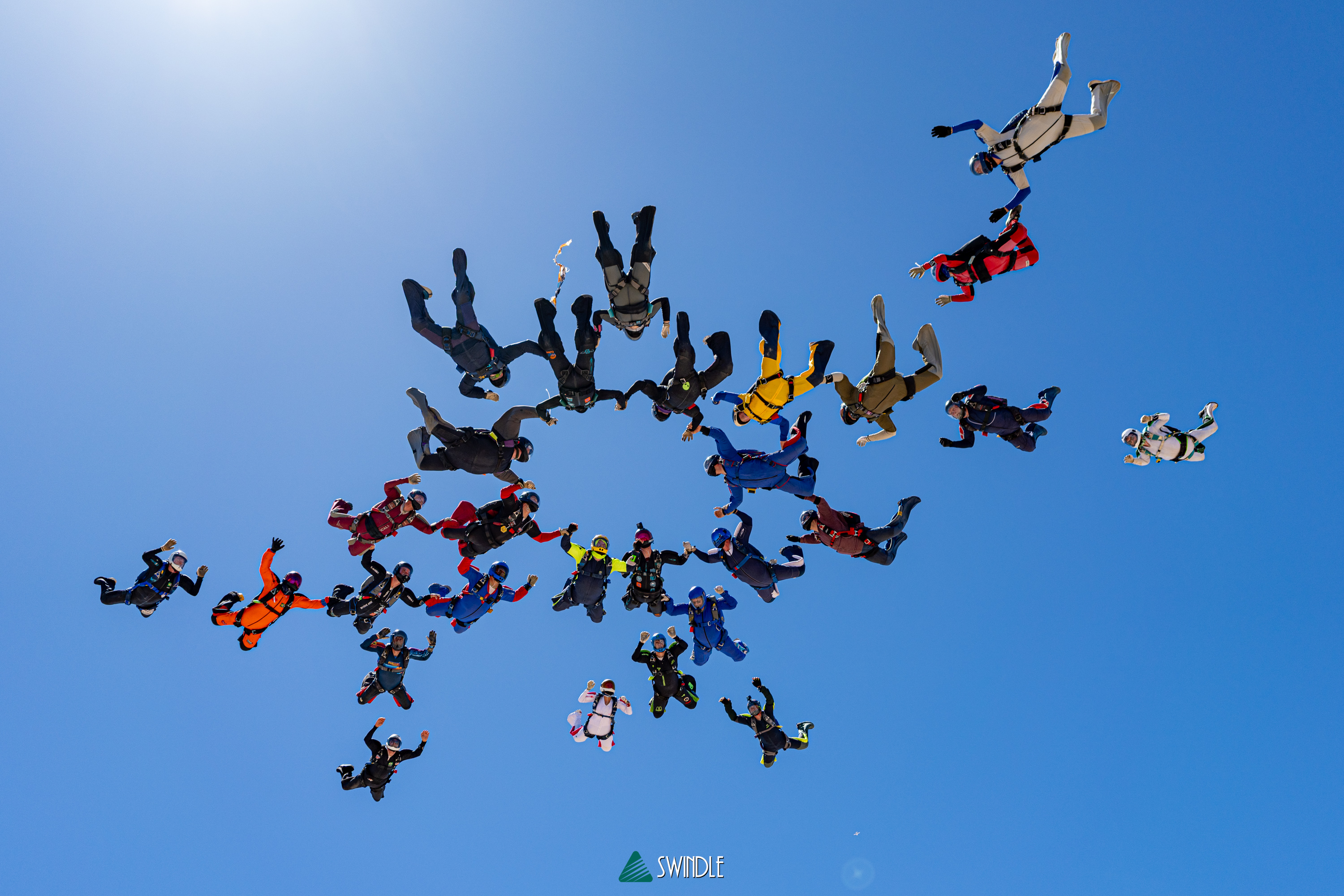 Skydivers forming a bright cluster against a blue sky