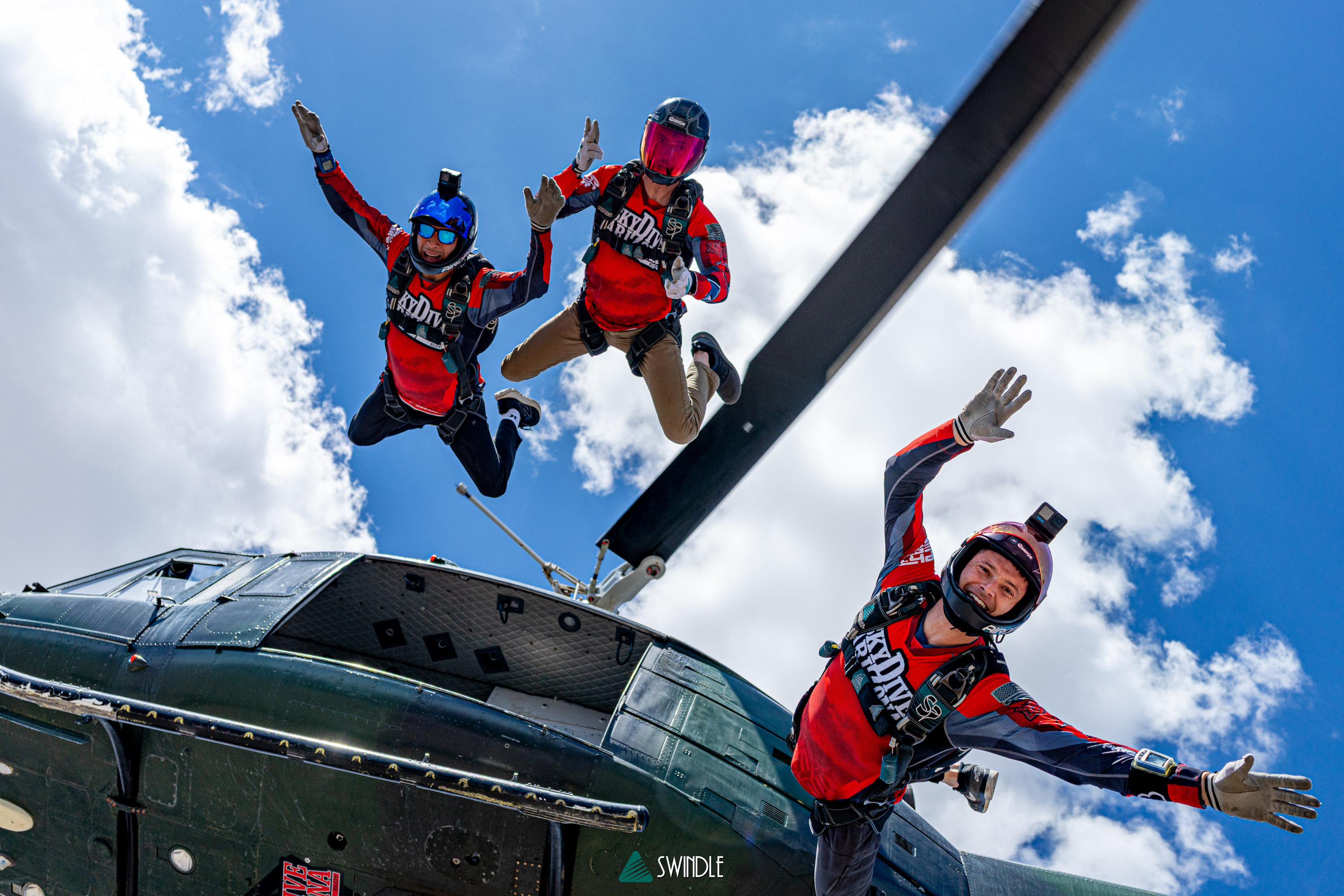 Doug Hendrix flying beside a jump plane with two other skydivers against a bright blue sky